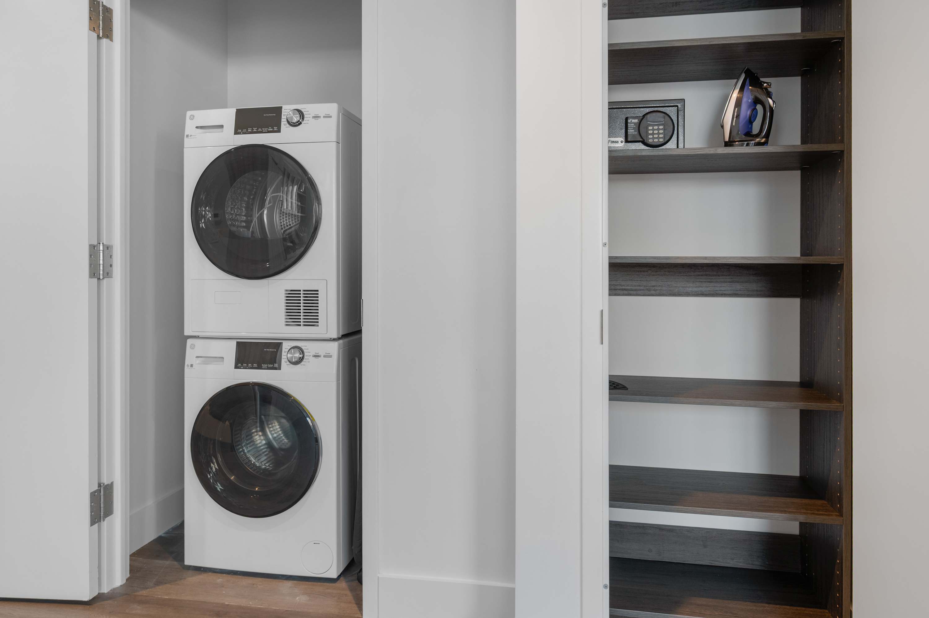 A white laundry room with a stacked washer and dryer and open shelves.