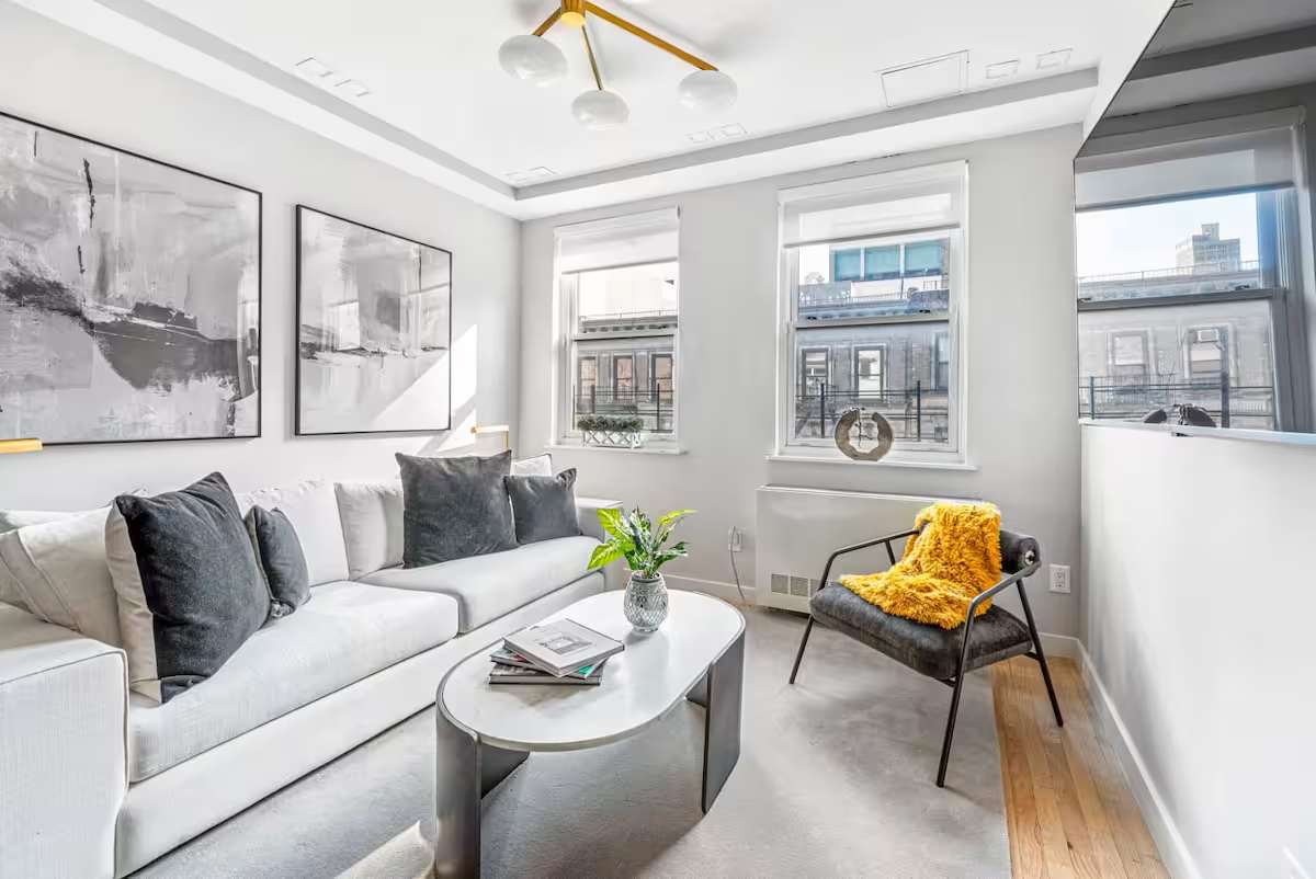 Living room with a white couch, coffee table, and large windows in a multi-bedroom apartment on East 62nd Street.