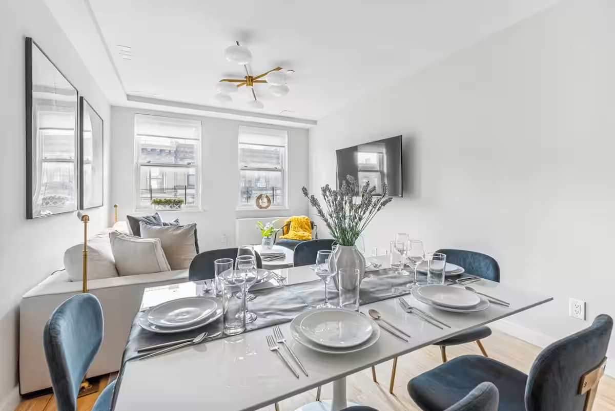 Dining table set for a meal with blue chairs and a white couch behind it in an East 62nd Street apartment.