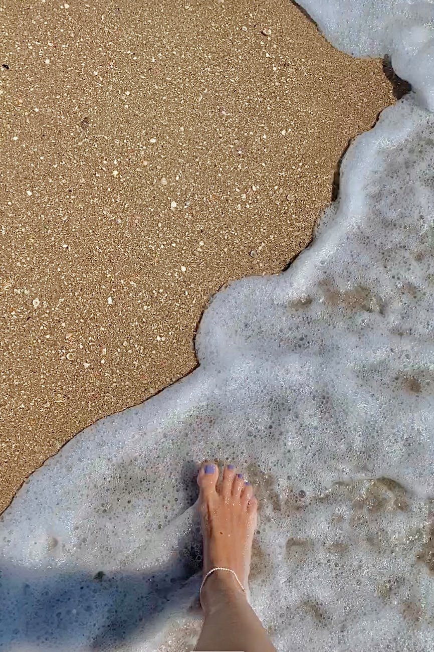 A bare foot at the edge of the water on our dark volcanic sand beach