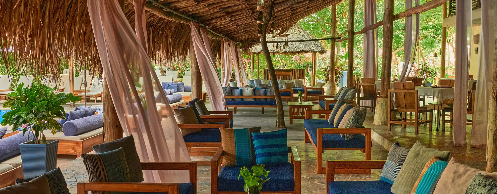 Restaurante al aire libre con muebles de madera y cortinas rosas