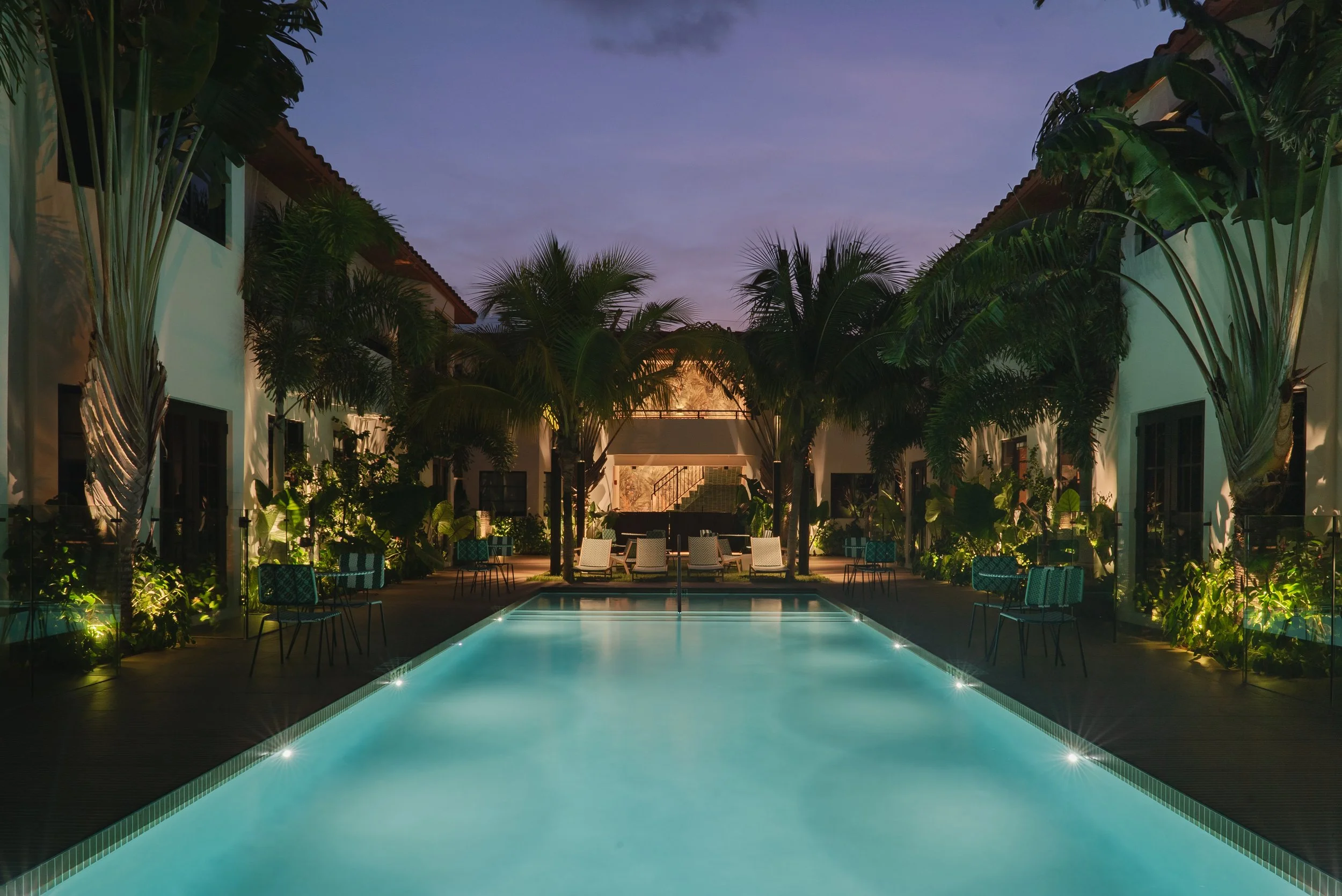 The outdoor courtyard pool at night, ringed with palms and loungers.