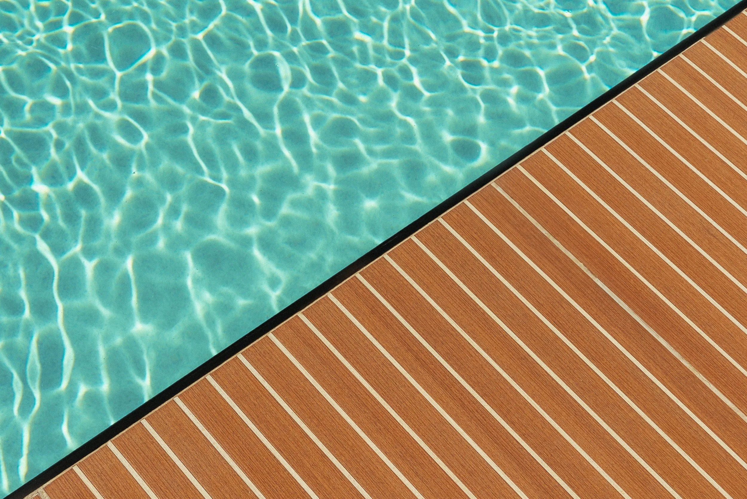 Detalle cercano de la tarima de teca rayada junto al agua de la piscina del patio
