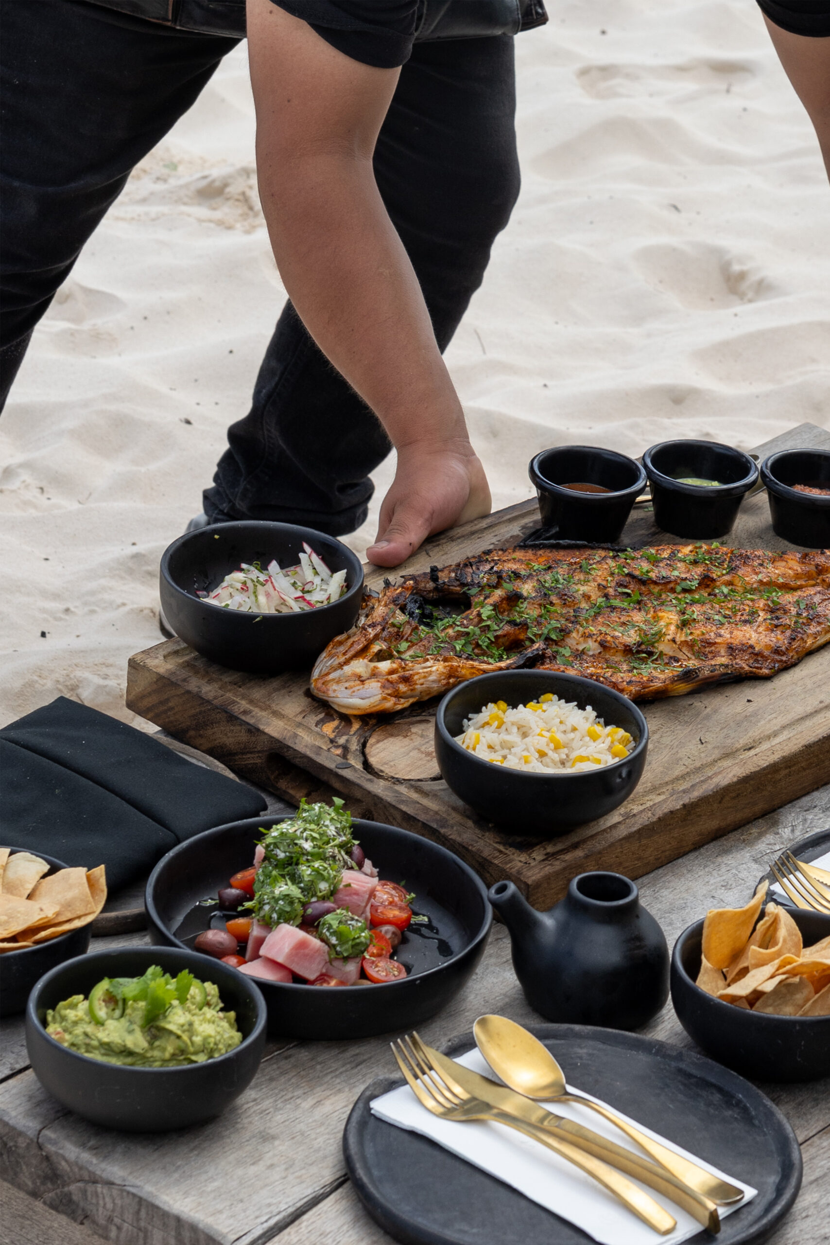 Grilled fish on a wooden board with sides, served on the sand