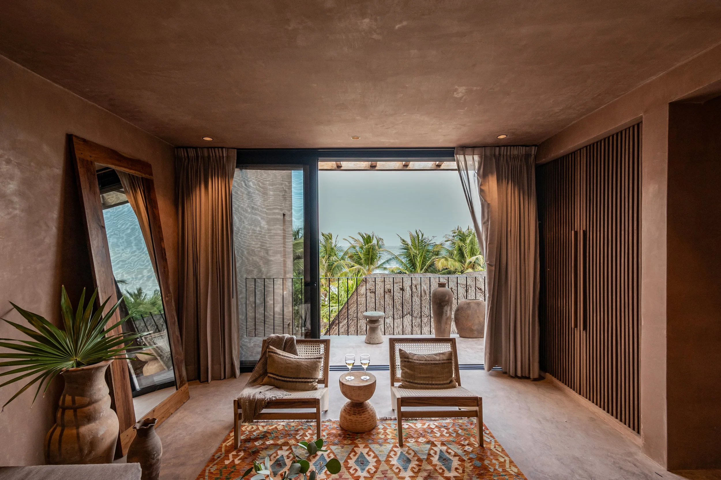 Suite living room opening onto a balcony with views of the ocean and greenery at XELA Tulum