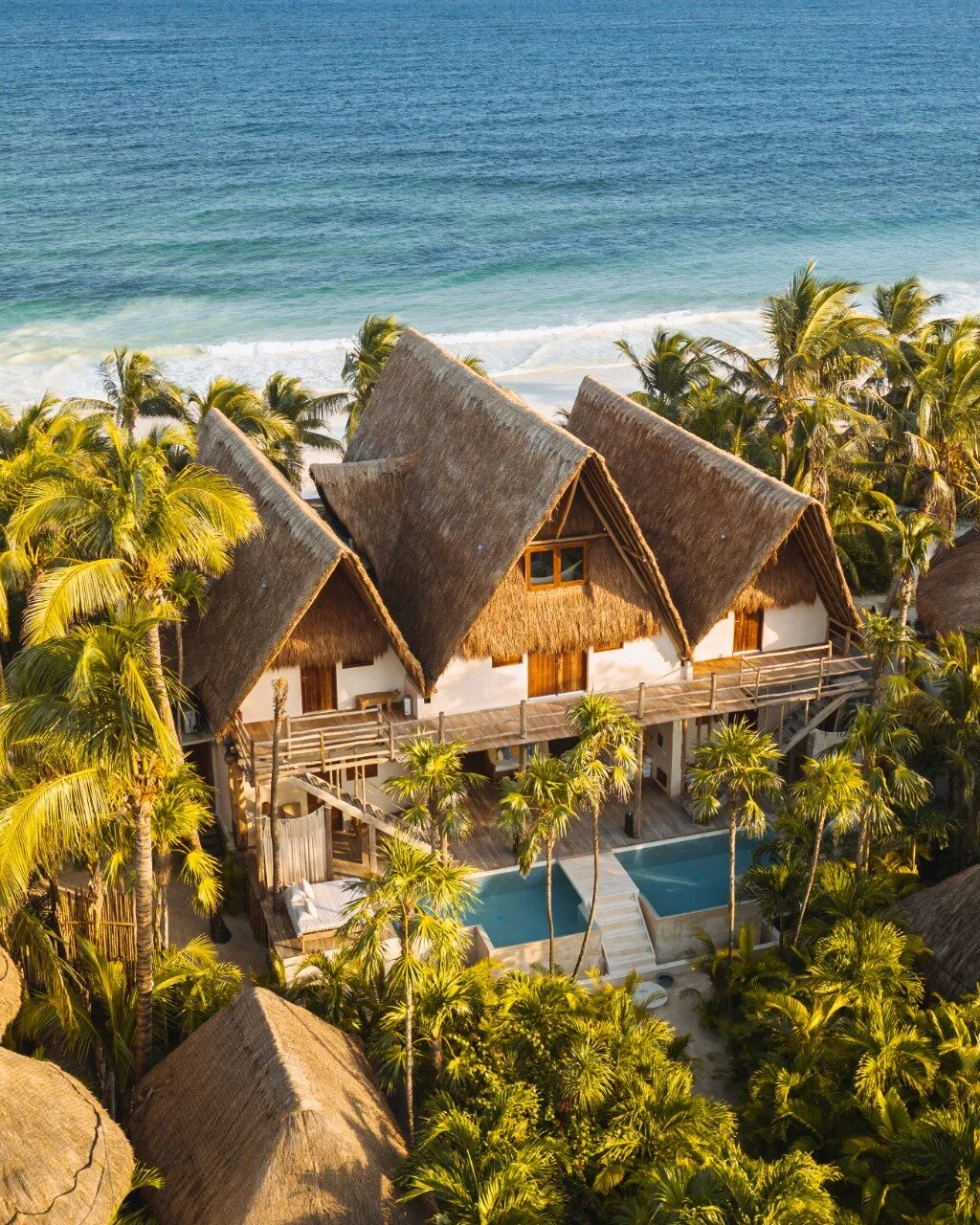 Aerial view of thatched beachfront villas among palms on Tulum Beach