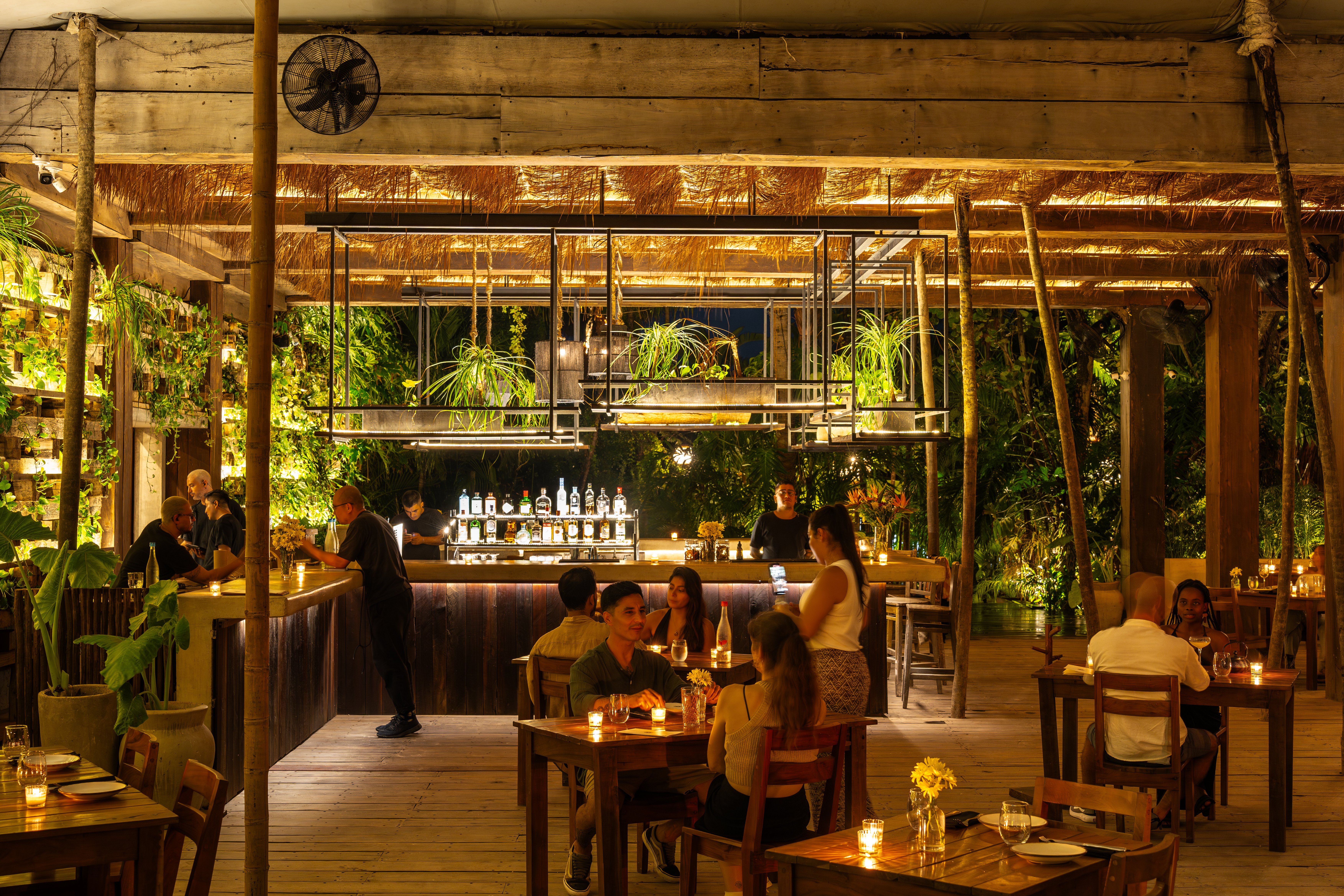 Guests dining by candlelight around the central bar at NÜ Tulum