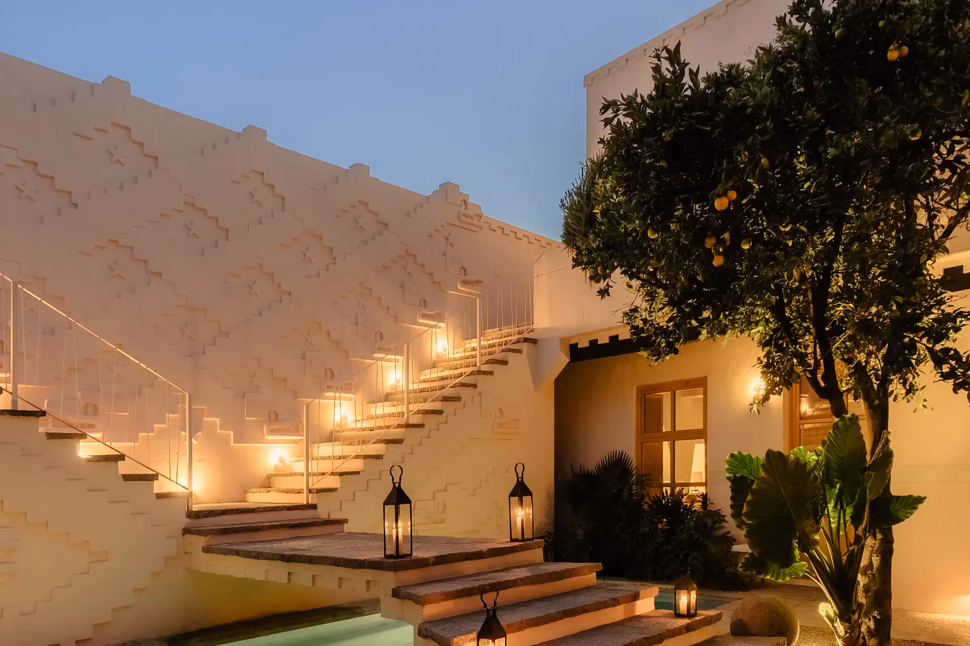 Lantern-lit staircase, pool and lemon tree in the courtyard at dusk at La Valise San Miguel de Allende